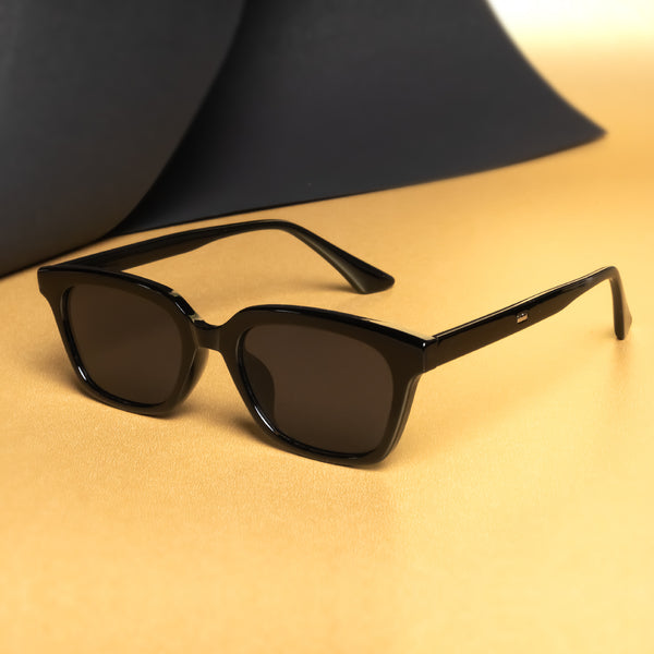 A pair of full black rectangle sunglasses with a matte finish, displayed on a surface with a dark object in the background.