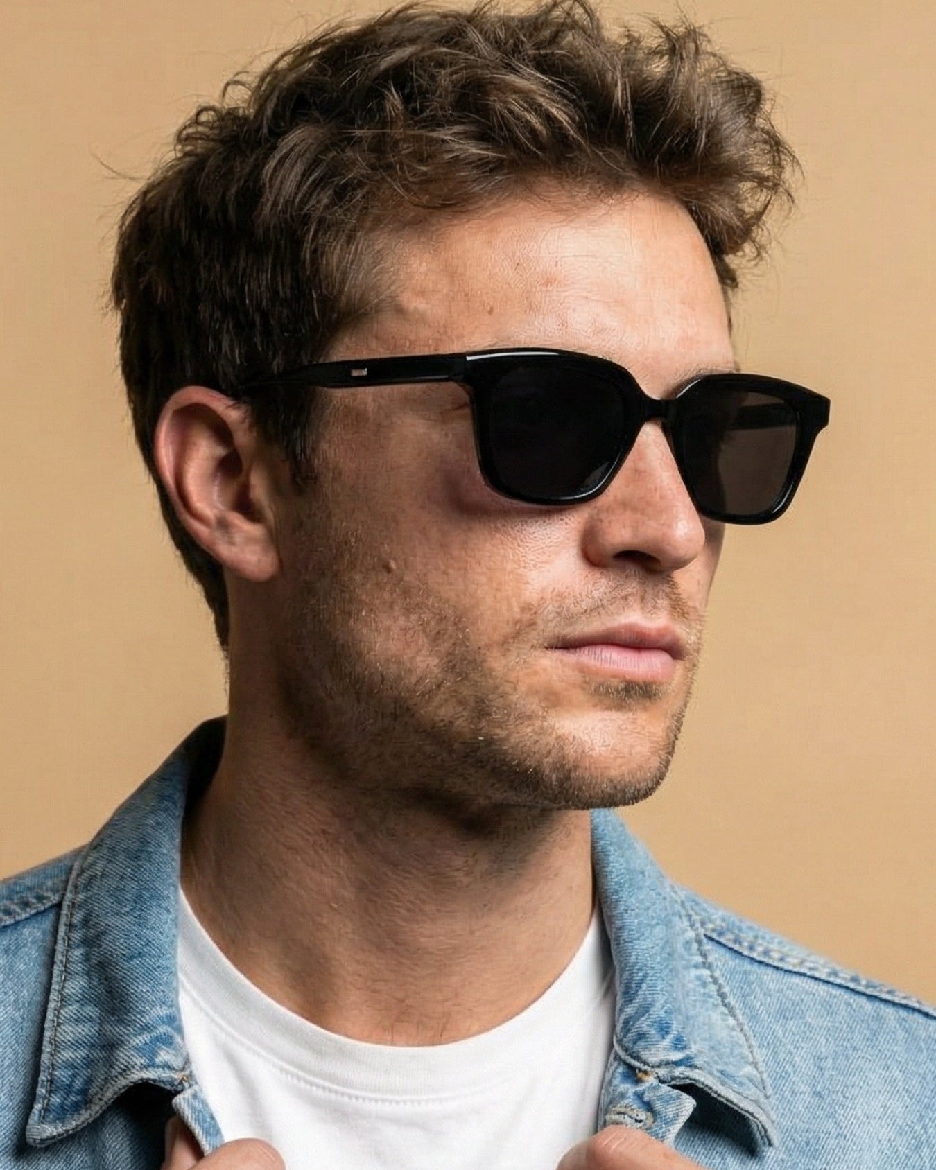 Man wearing black sunglasses and a denim jacket against a beige background