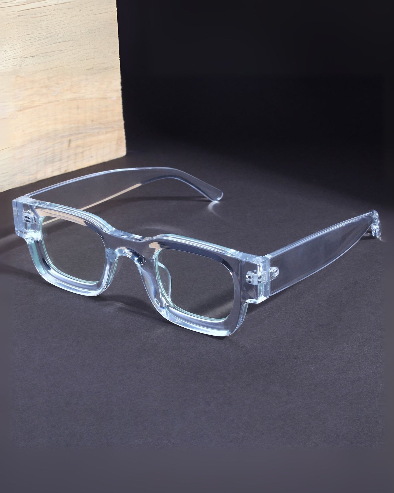 Clear eyeglasses on a dark surface with a light wooden block in the background