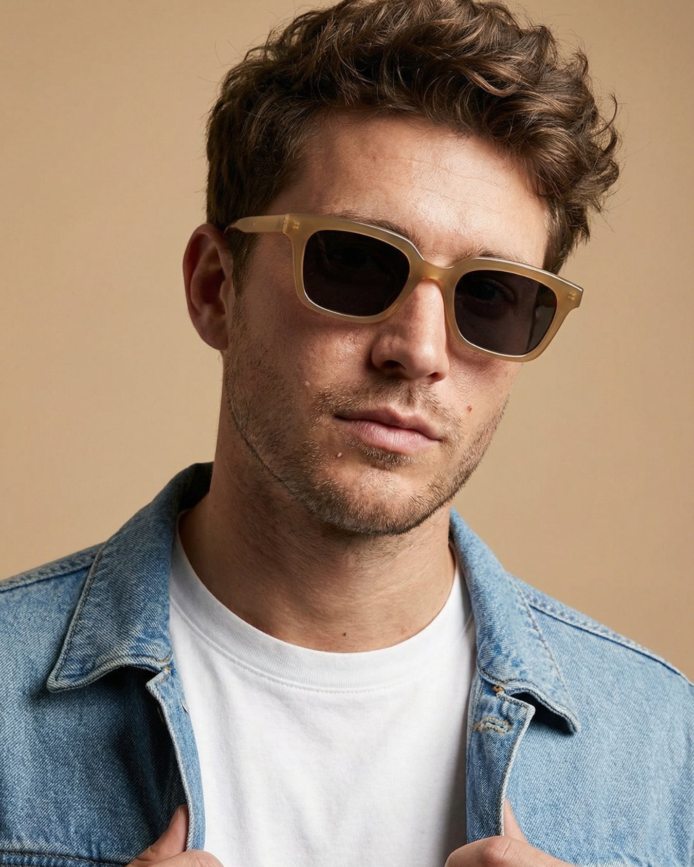 Man wearing sunglasses and a denim jacket against a beige background