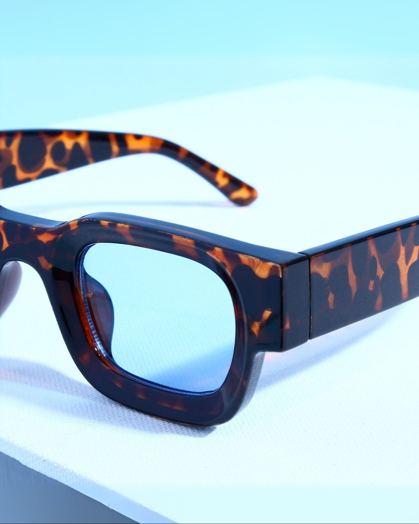 Sunglasses with tortoiseshell frame and blue lenses on a light blue background