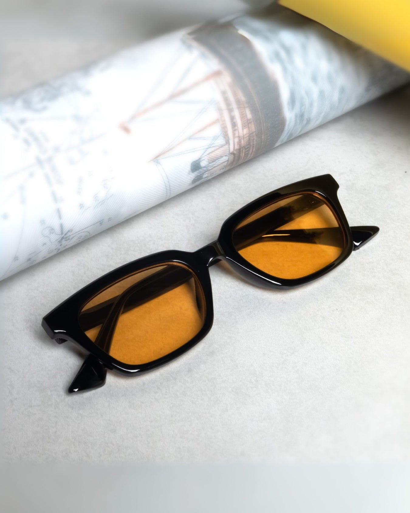 Sunglasses with orange lenses and black frame on a light gray surface.