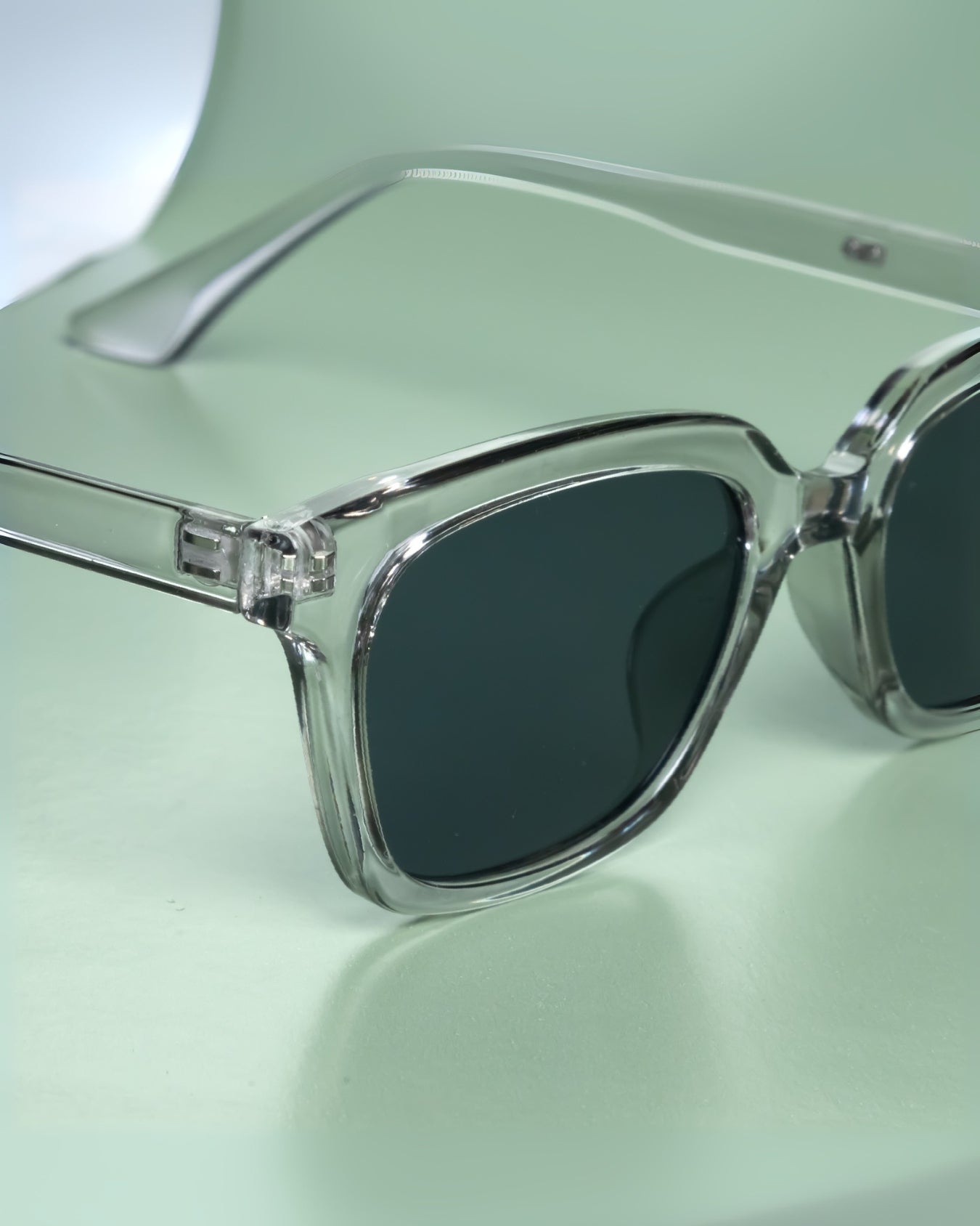 Sunglasses with clear frame and dark lenses on a light green background