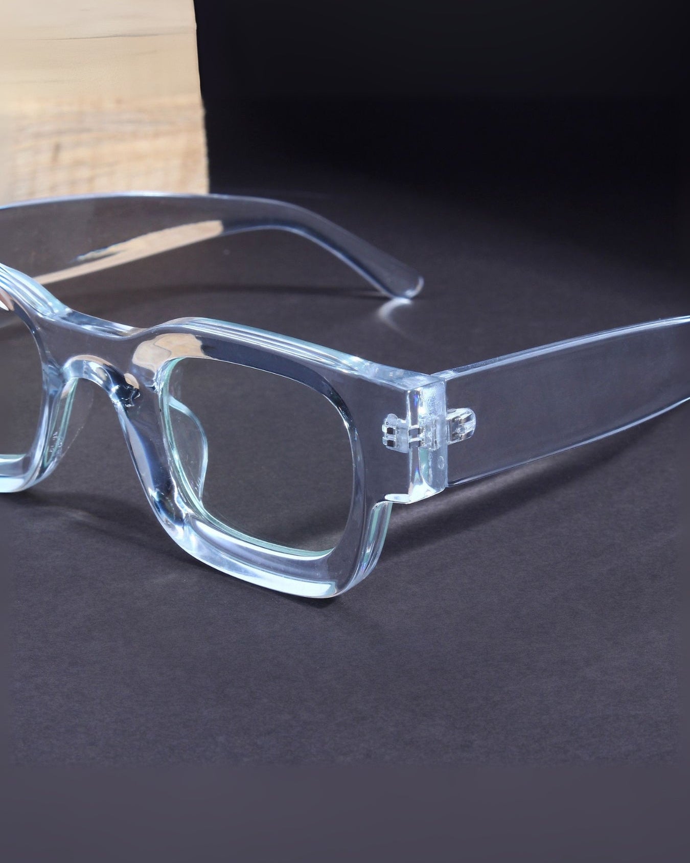 Clear eyeglasses on a dark surface with a wooden background