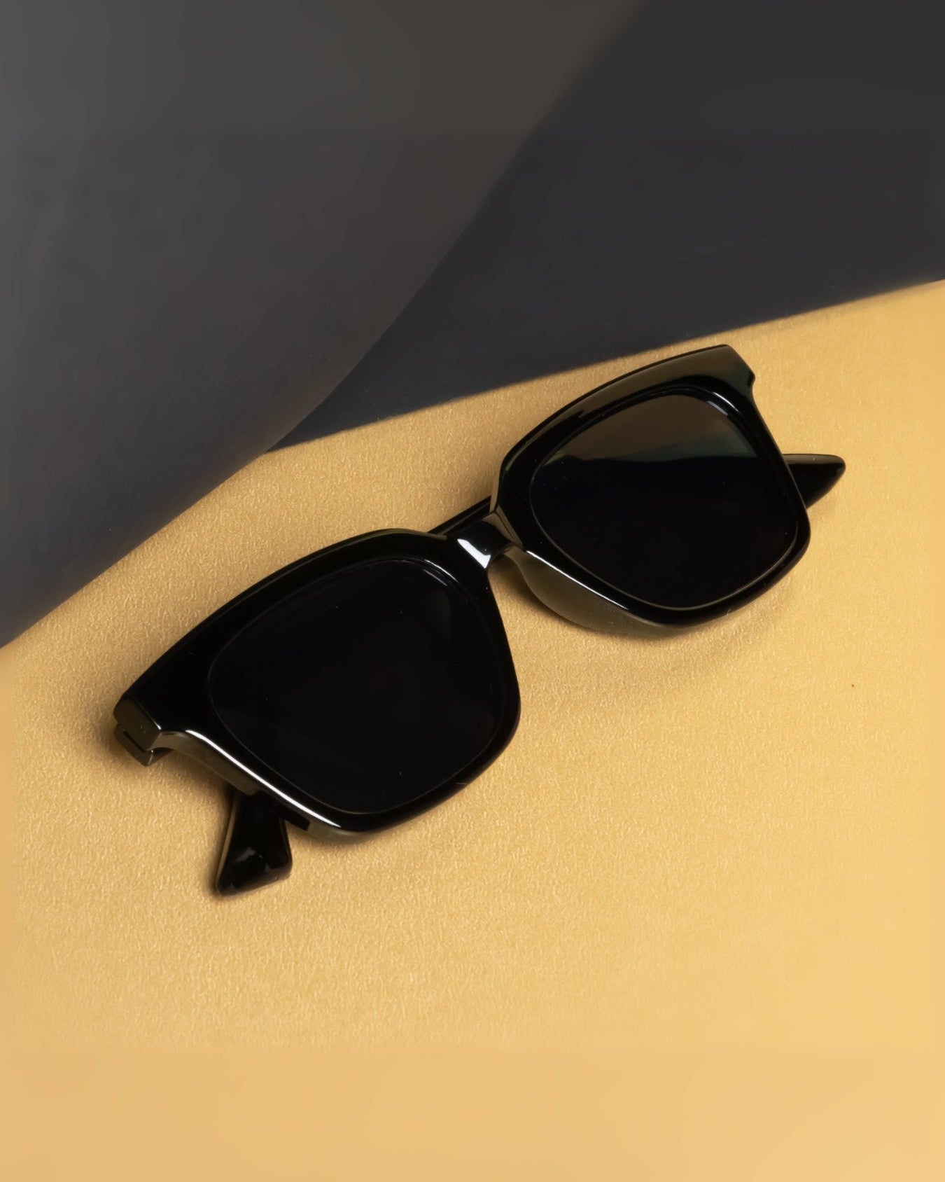 Black sunglasses on a beige surface with a dark background