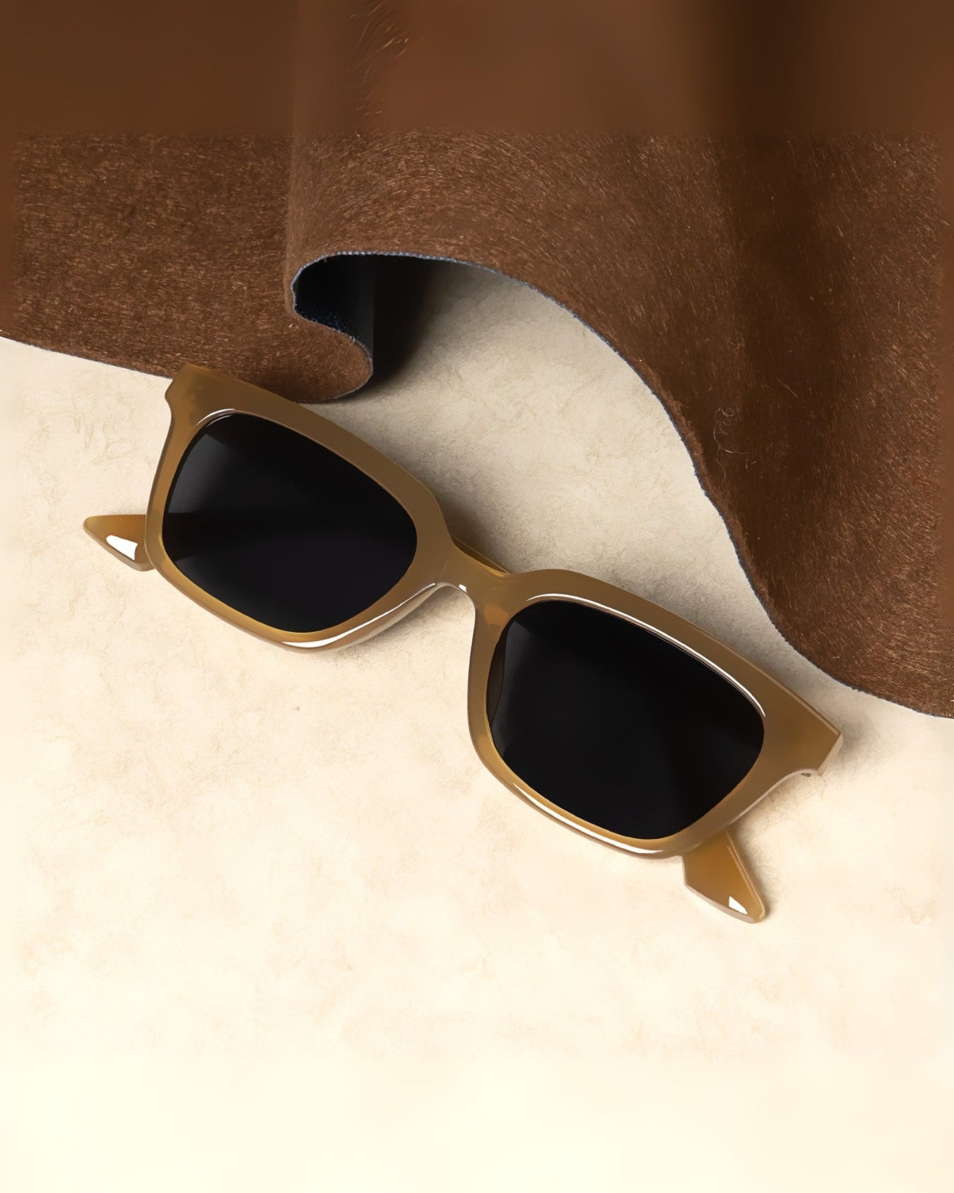 Gold-framed sunglasses with black lenses on a beige surface with brown fabric in the background