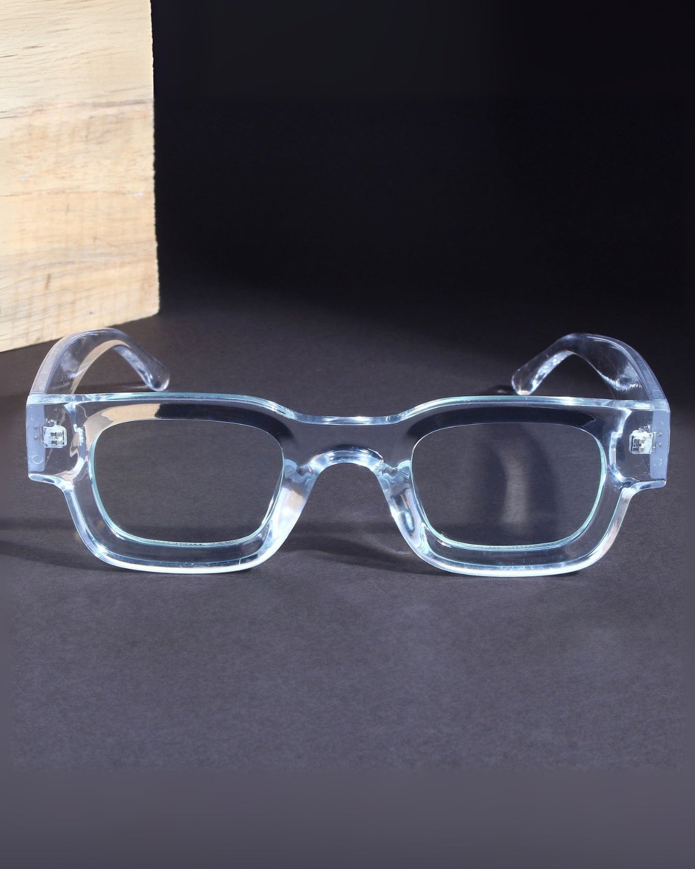 Clear eyeglasses on a dark surface with a wooden block in the background