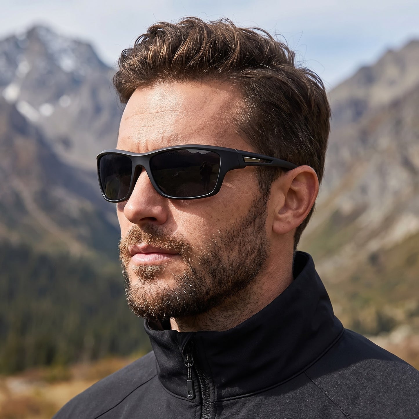 A man wearing black athletic sunglasses with a gold accent on the temple, set against a blurred mountain landscape.