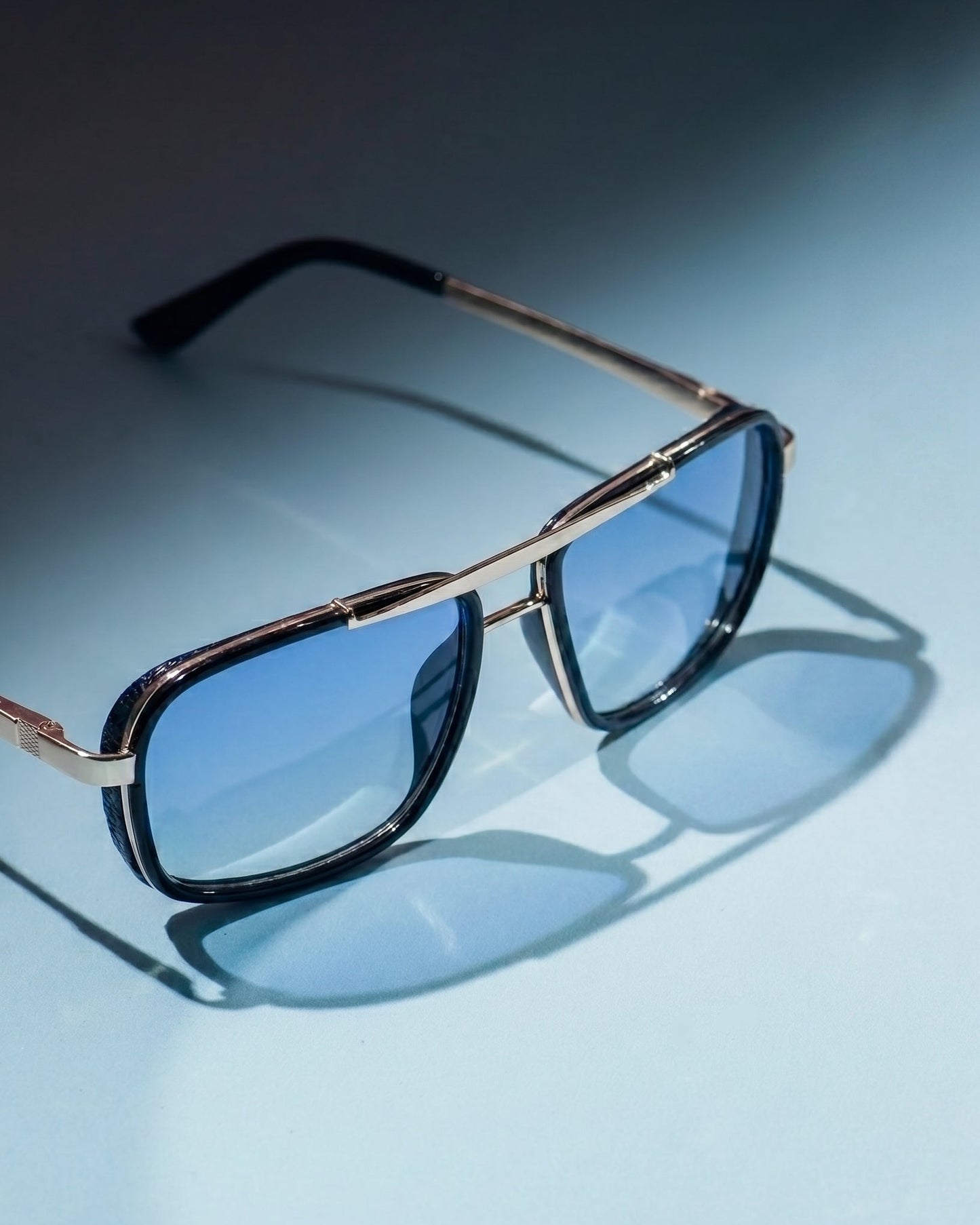Sunglasses with gold frame and blue lenses on a light blue background